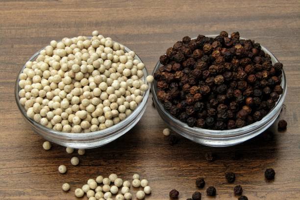 White pepper and black pepper in bowl on wooden background